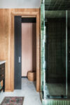 Modern mountain homes bathroom shower detail with green tile, glass enclosure, wood doorway, dark vanity, and patterned rug