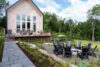 Back view of a contemporary mountain home in the Hudson Valley featuring a modern campfire pit, lounge chairs, and forest surroundings.