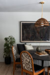 Modern mountain homes dining area with patterned chairs, round table, woven pendant light, framed artwork, and greenery