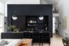 Modern mountain home interior with black built-in kitchen cabinetry, counter-height bar seating, high ceiling, wood table, and lounge seating