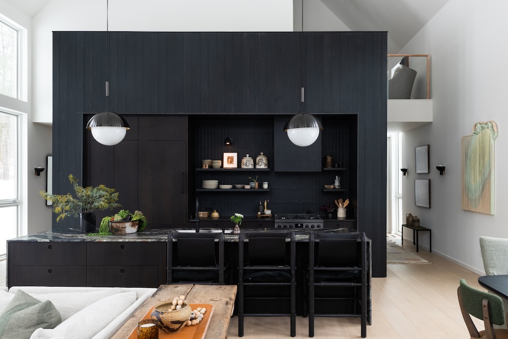 Modern mountain home interior with black built-in kitchen cabinetry, counter-height bar seating, high ceiling, wood table, and lounge seating
