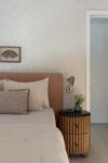 Modern mountain homes bedroom detail with upholstered bed, layered pillows, wood nightstand, wall sconce, and framed art
