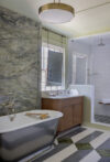 Freestanding tub, wood cabinetry, patterned floor, window, and light stone wall detail