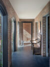 Brick hallway with arched openings, dark floor, bench seating, and stair view