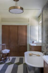 Bathroom with freestanding tub, wood cabinetry, patterned floor, window, and light stone wall detail