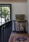 Landing with small writing desk, black railing, large window, framed art, and patterned rug
