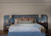 Custom blue headboard with vintage nightstands and built in sconces make this coastal primary bedroom elegant and luxurious.