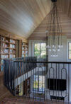 Coastal interiors staircase landing with wood ceiling, black railing, bookshelves, and pendant light