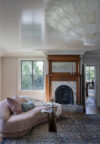 Vintage fireplace and modern curved sofa featured in sitting area of luxury primary bedroom with water front views.