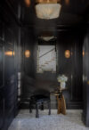 Modern mountain homes entry hall with dark paneled walls, bench seating, wall sconces, mirror, and patterned floor