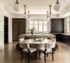 Elegant luxury kitchen featuring a custom upholstered banquette, round dining table, dark wood cabinetry, white tile walls, and brass globe pendant lighting in a modern classic luxury kitchen.