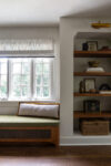 Sunlit wall with built-in wooden bookshelves and a bench in a renovated Westfield Tudor Revival home.