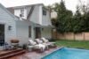 Back exterior of modern ranch home in Westfield NJ with white facade, swimming pool, and poolside lounge chairs.