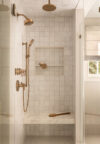 Bathroom shower with glass enclosure, tiled walls, built-in niche, bench, and brass-toned shower fixtures