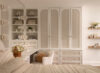 Vanity area with floor-to-ceiling built-in cabinetry, arched cabinet doors, open shelving, large mirror, day bed, and upholstered chair