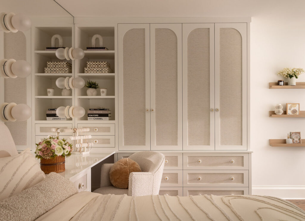 Vanity area with floor-to-ceiling built-in cabinetry, arched cabinet doors, open shelving, large mirror, day bed, and upholstered chair