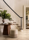 Luxury whole house renovation NJ foyer with curved wood entry table, floral arrangement, round stool, staircase, and doorway to living room