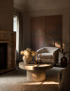 Fireplace seating area with round coffee table, upholstered chair, floral arrangement, and two dark wall artworks