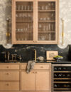 Luxury whole house renovation NJ home bar with glass-front cabinets, dark counter and backsplash, brass faucet, wall sconces, and built-in wine storage