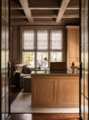 Luxury whole house renovation NJ home office with wood paneled desk, wood cabinetry, patterned window shades, dark frosted glass paneled doors, and coffered ceiling