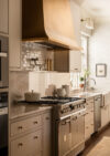 Whole house renovation NJ kitchen range with warm-toned hood, tiled backsplash, paneled drawers, and sunlit sink area
