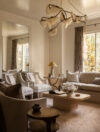 Luxury whole house renovation NJ living room with curved sofa, upholstered chairs, sculptural chandelier, wood coffee table, oversized wall mirror, and full-length dark neutral drapery panels