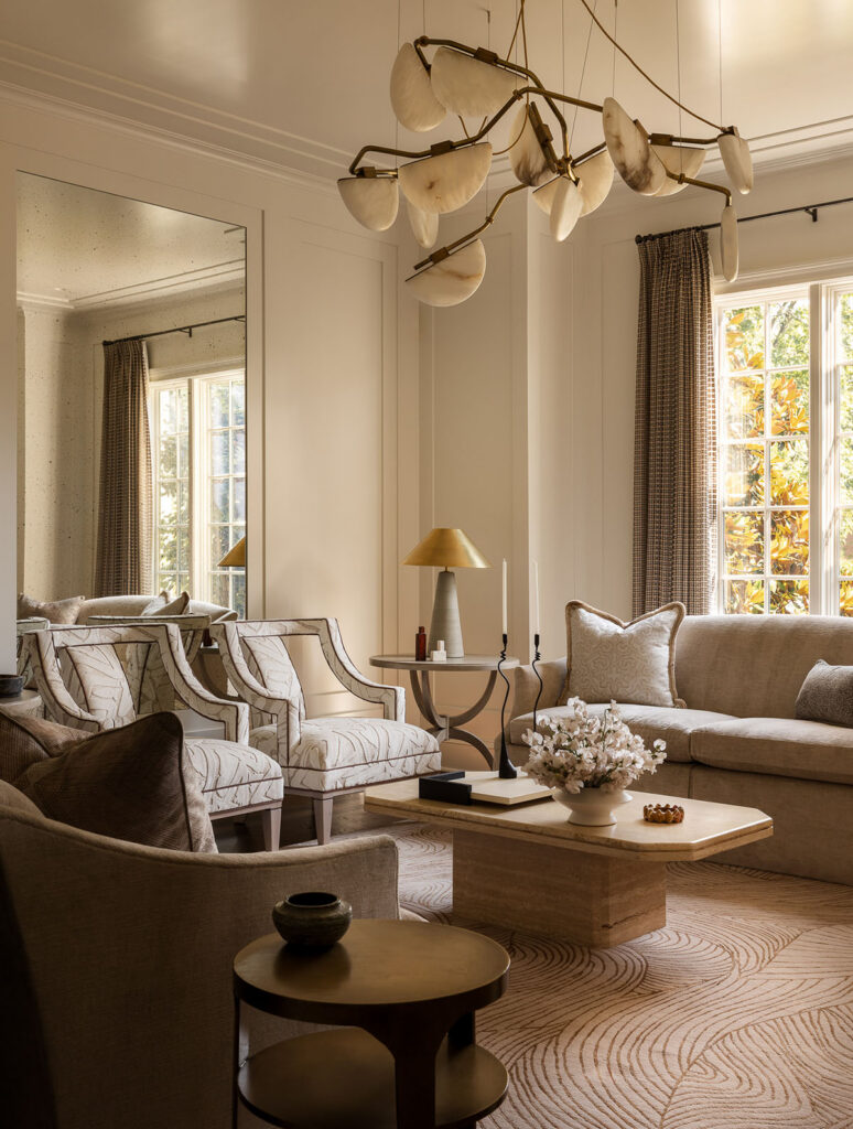 Luxury whole house renovation NJ living room with curved sofa, upholstered chairs, sculptural chandelier, wood coffee table, oversized wall mirror, and full-length dark neutral drapery panels