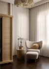 Luxury whole house renovation NJ seating area with upholstered lounge chair, round side table, tall sheer drapery, pendant lighting, and wood cabinet