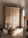 Seating area with tall wood cabinet, round coffee table, fireplace, upholstered chairs, and soft natural light
