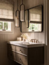 Bathroom sink area with wood vanity, rectangular mirror, pendant lighting fixtures, marble countertop, roman shades, and brass-toned fixtures