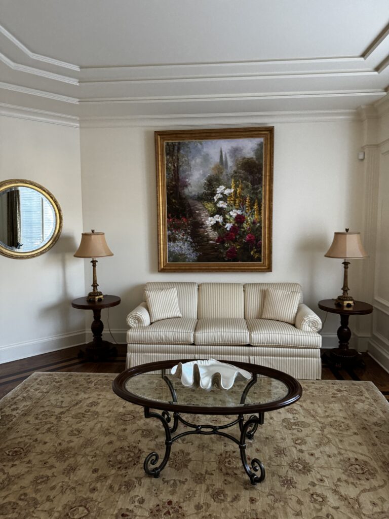 before image of a traditional living room with striped sofa, dark wood coffee table, framed artwork, area rug, and classic furniture