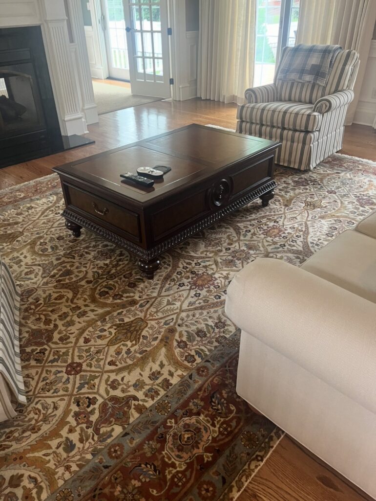 before image of traditional living room with striped armchair dark wood coffee table patterned rug and fireplace