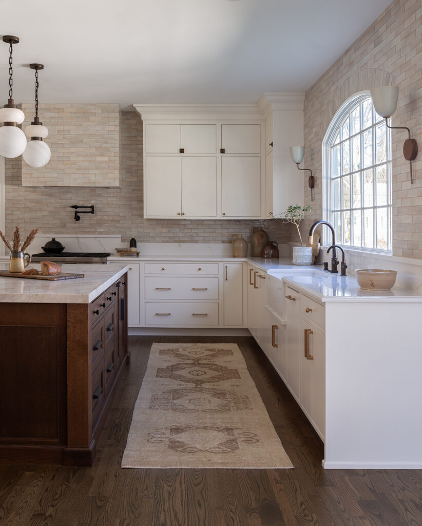 Luxury kitchen with white cabinetry, stone backsplash, large island, arched window, and brass hardware