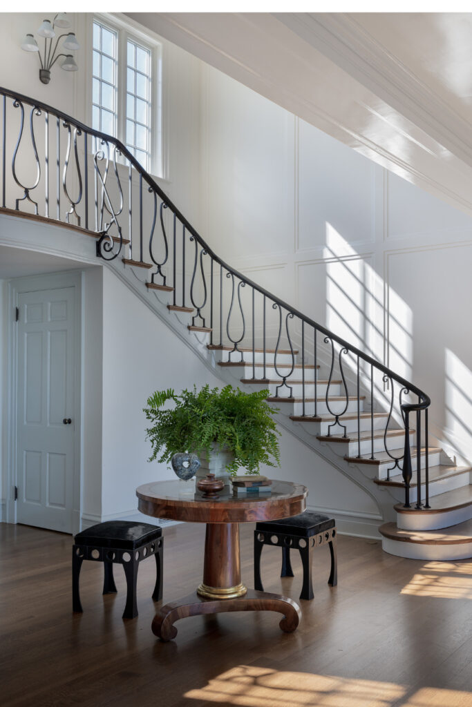 Elegant entryway with curved staircase, black iron railing, white walls, and natural light