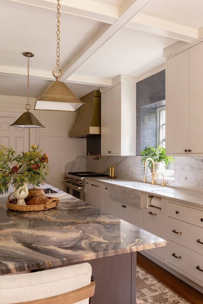 Luxury kitchen with marble island countertop, white cabinetry, brass fixtures, and statement pendant lighting