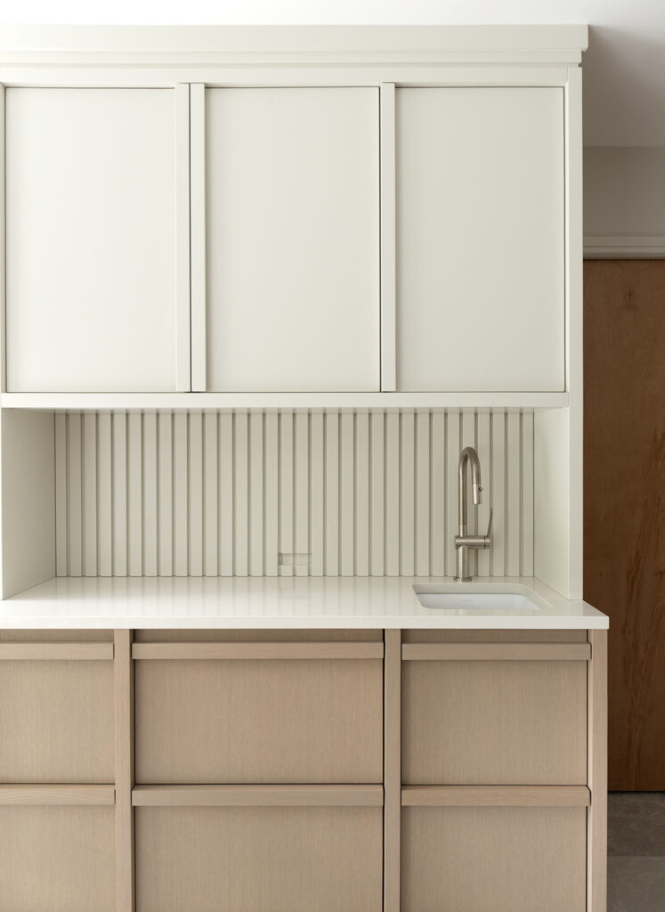 Custom beverage station with white cabinetry, integrated sink, and fluted backsplash detail