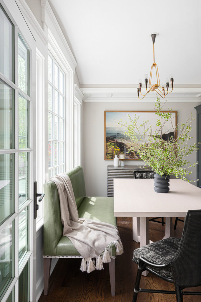 Bright kitchen in Westfield, New Jersey featuring a long table with bench seating, expansive windows letting in sunlight, and an ocean painting on the wall.